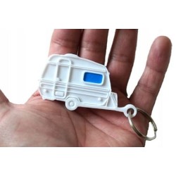 Brelok w kształcie białej mini przyczepy kempingowej Niewiadów N126N z jasnoniebieskim oknem prezentowany na dłoni